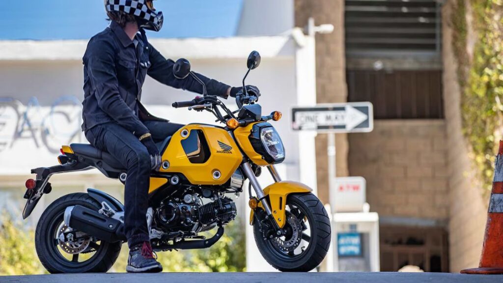 a rider sitting on his honda grom in front of a fuel pump